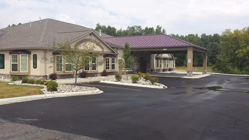 Front exterior of a senior living building with a covered entrance/porte-cochere, landscaped beds, and a paved driveway.