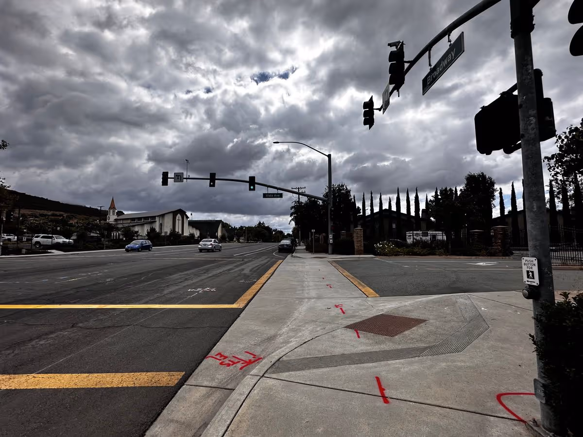 Cloudy street intersection with traffic lights, crosswalk markings, and a church building in the distance.