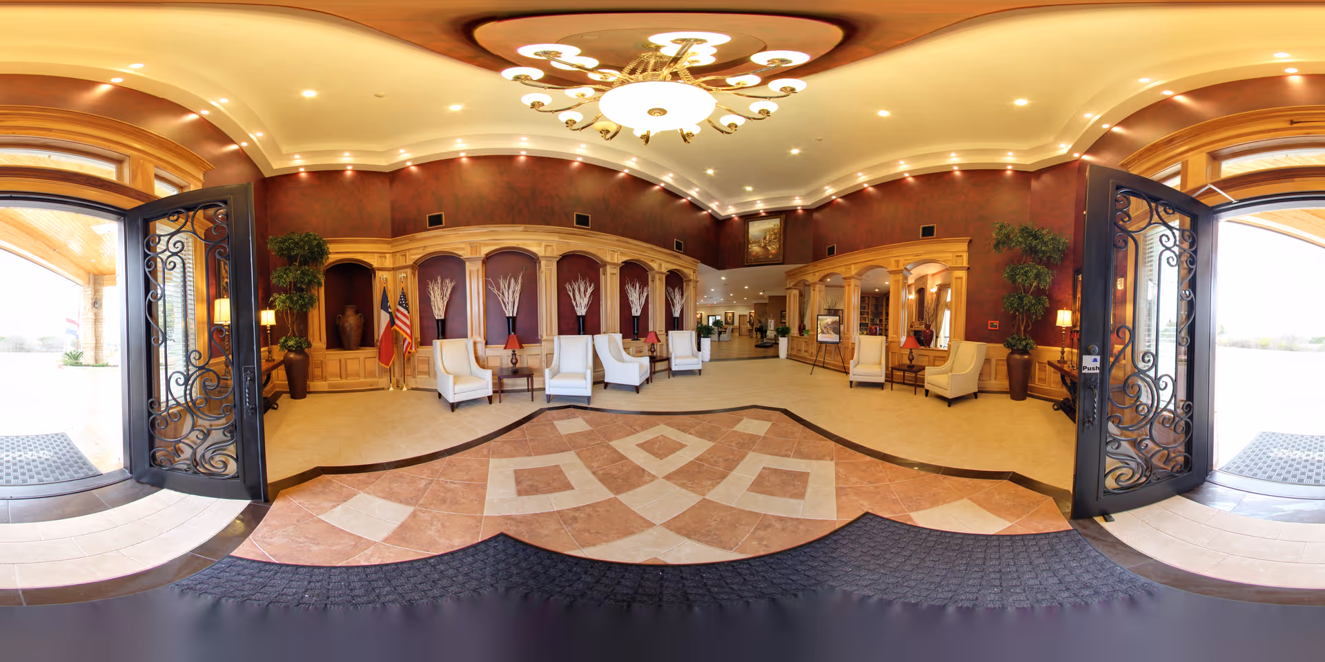 Wide, elegant assisted-living lobby with open ornate double doors, tiled floor, chandelier, and several seating areas against wood-paneled walls.