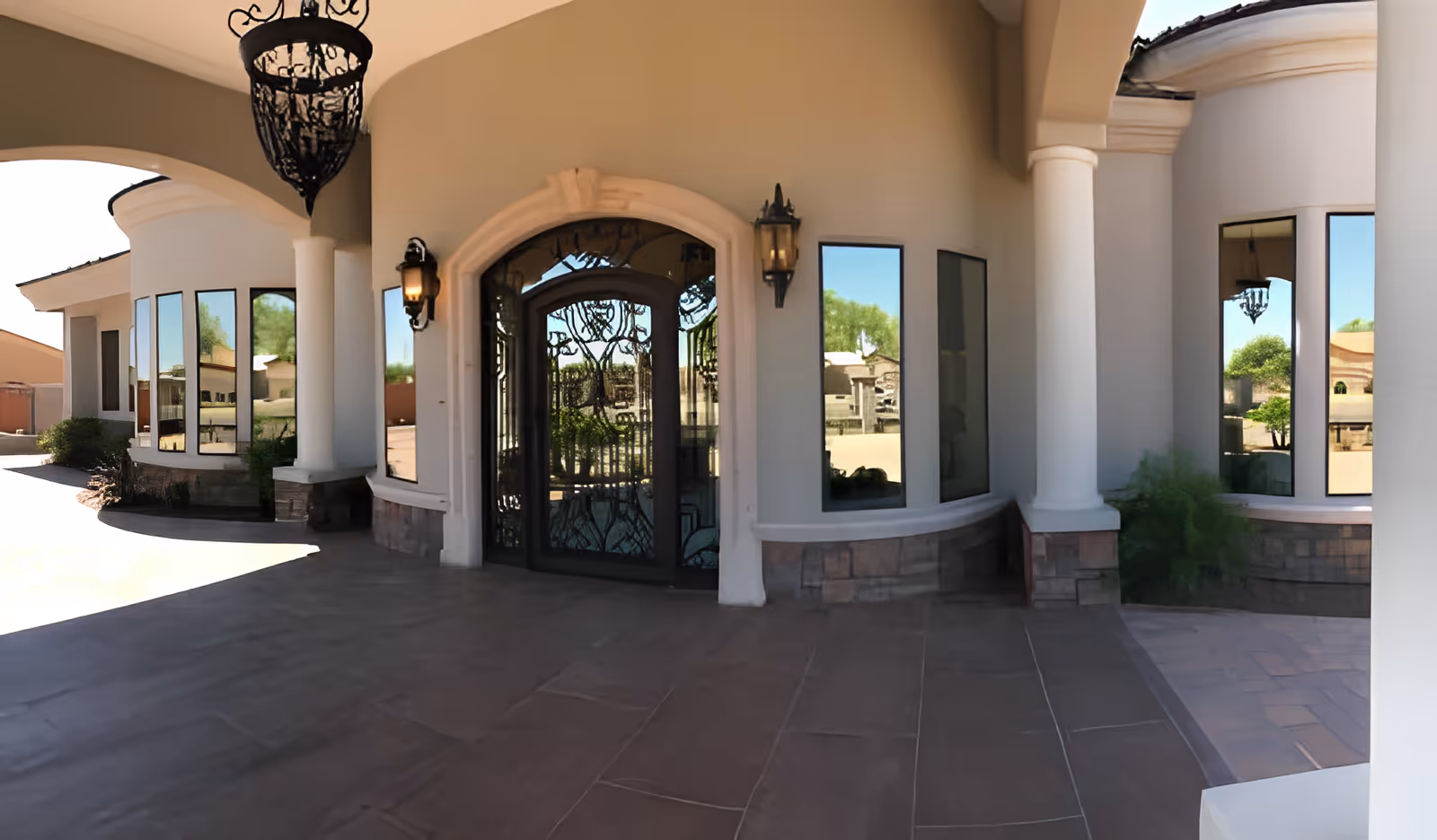 Front entrance with arched wrought-iron double doors, columns, large windows, and a covered portico.