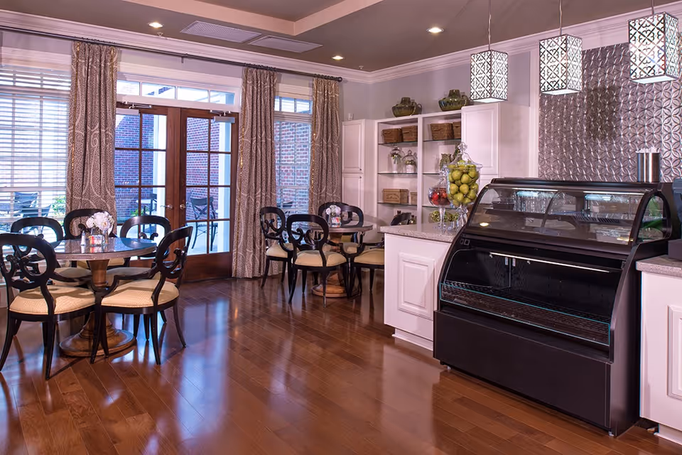 Bright dining area with round tables and chairs, a glass display case, shelving, and double doors leading to an outdoor patio.