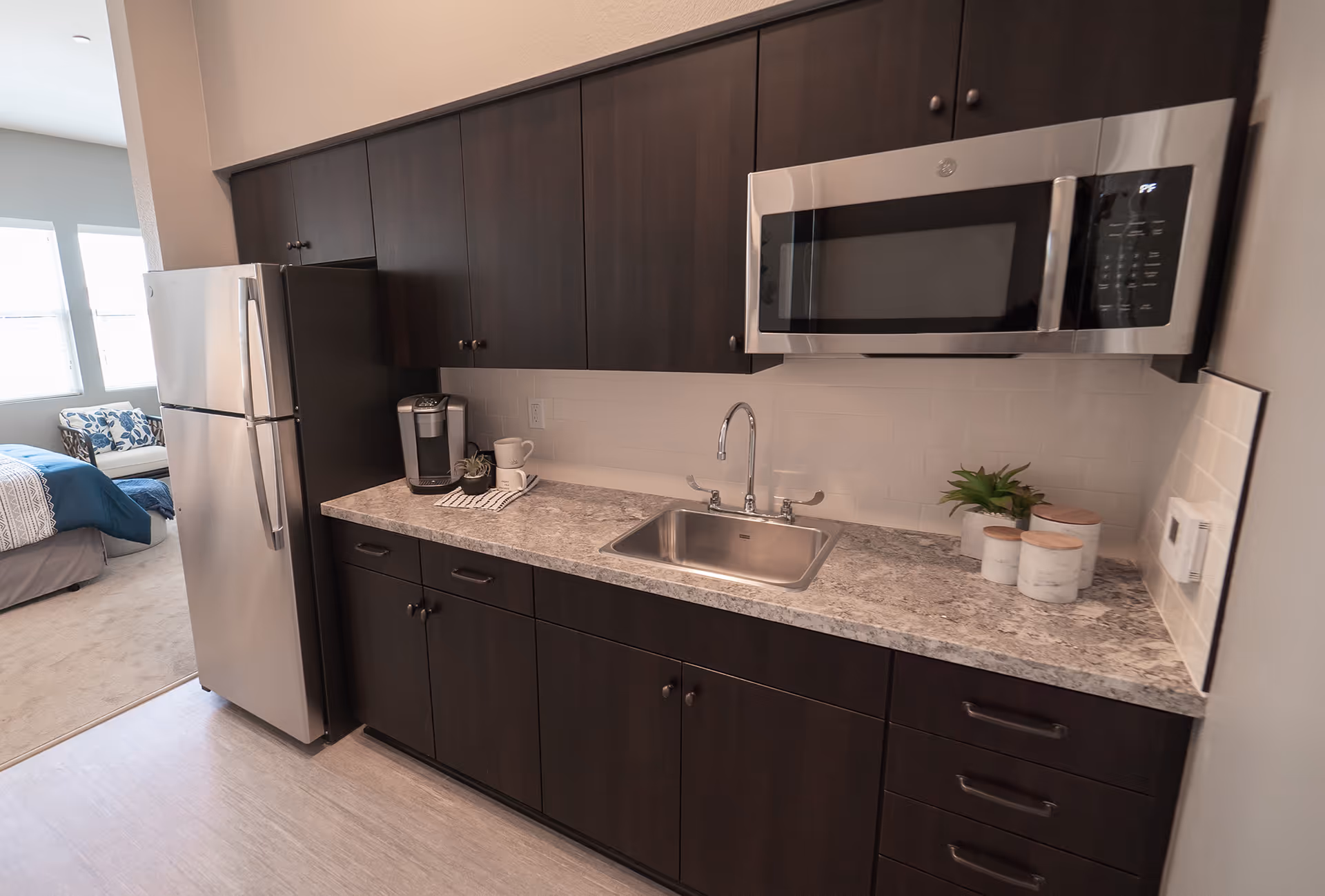Small modern kitchen with dark cabinets, stainless steel refrigerator and microwave, a sink and countertop accessories