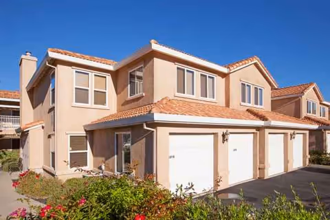 Exterior view of Atria Rocklin, beige two-story senior living complex with garages and red-tiled roof.