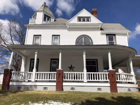 White two-story house-style senior living facility with a wraparound porch and columns.