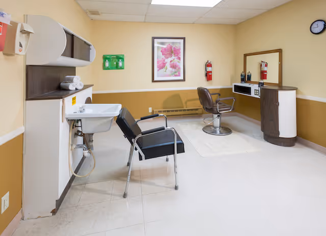 Salon-style interior with two styling chairs, a wash sink, mirror and small workstation against beige walls.