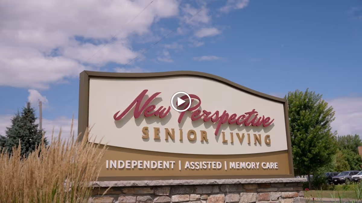 Large outdoor sign reading "New Perspective Senior Living" with services listed and landscaping and sky in the background.