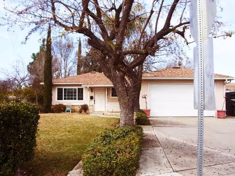 A single-story care home with a driveway, front yard, and large tree.