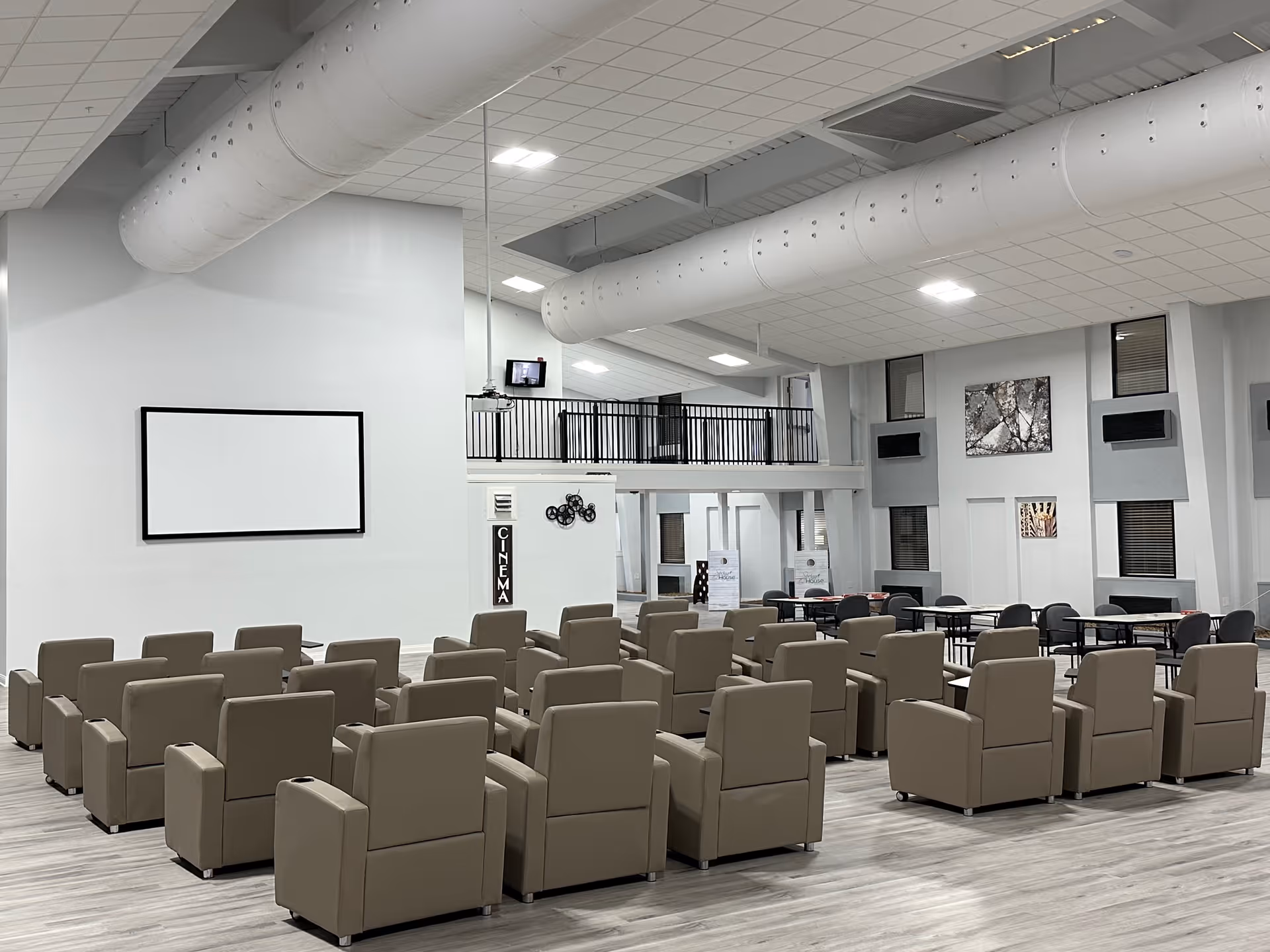 A large communal room with rows of beige recliner chairs facing a blank wall-mounted projection screen in a senior living facility.