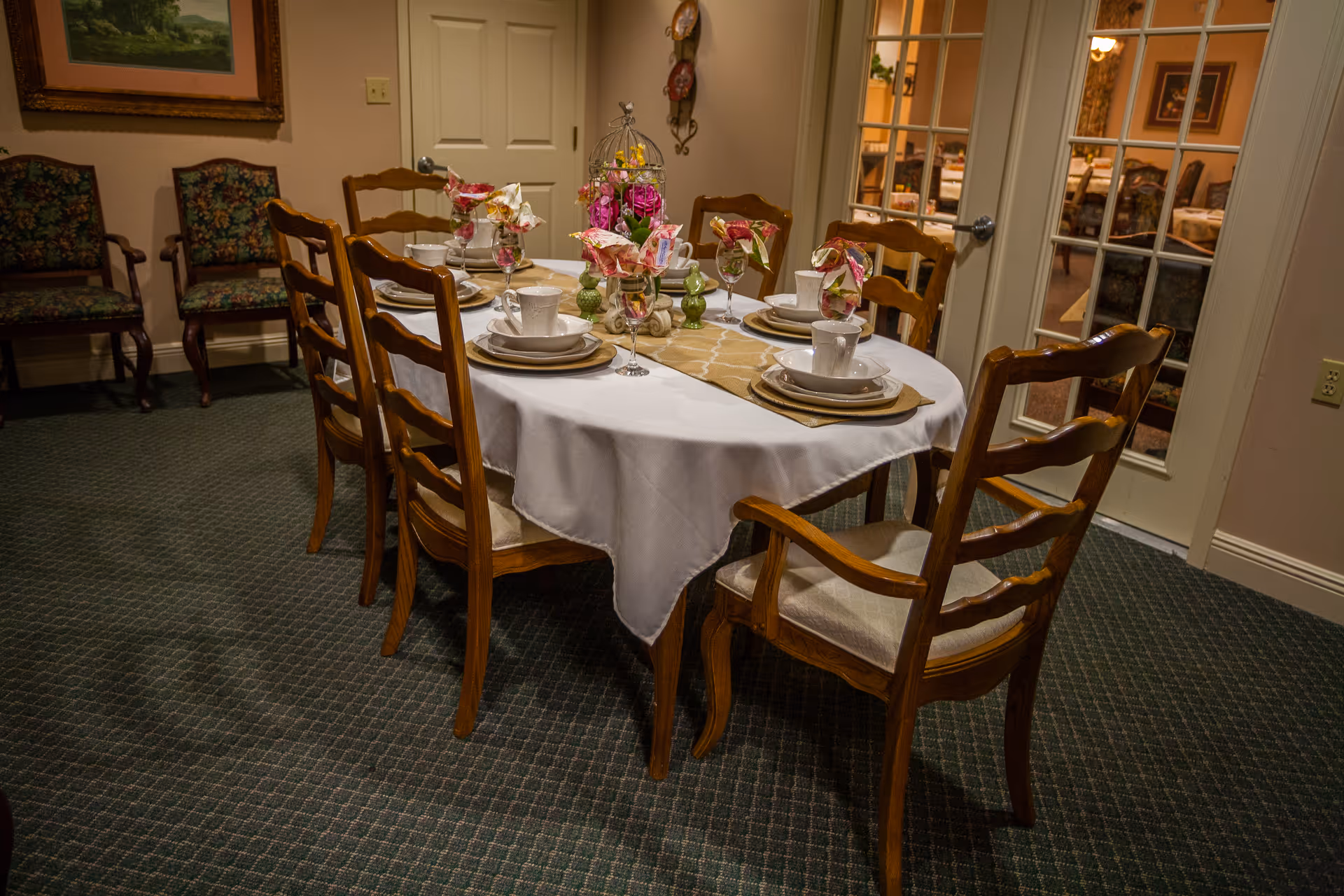 A dining room with a round table set for six, wooden chairs, plates, cups, and floral centerpieces.