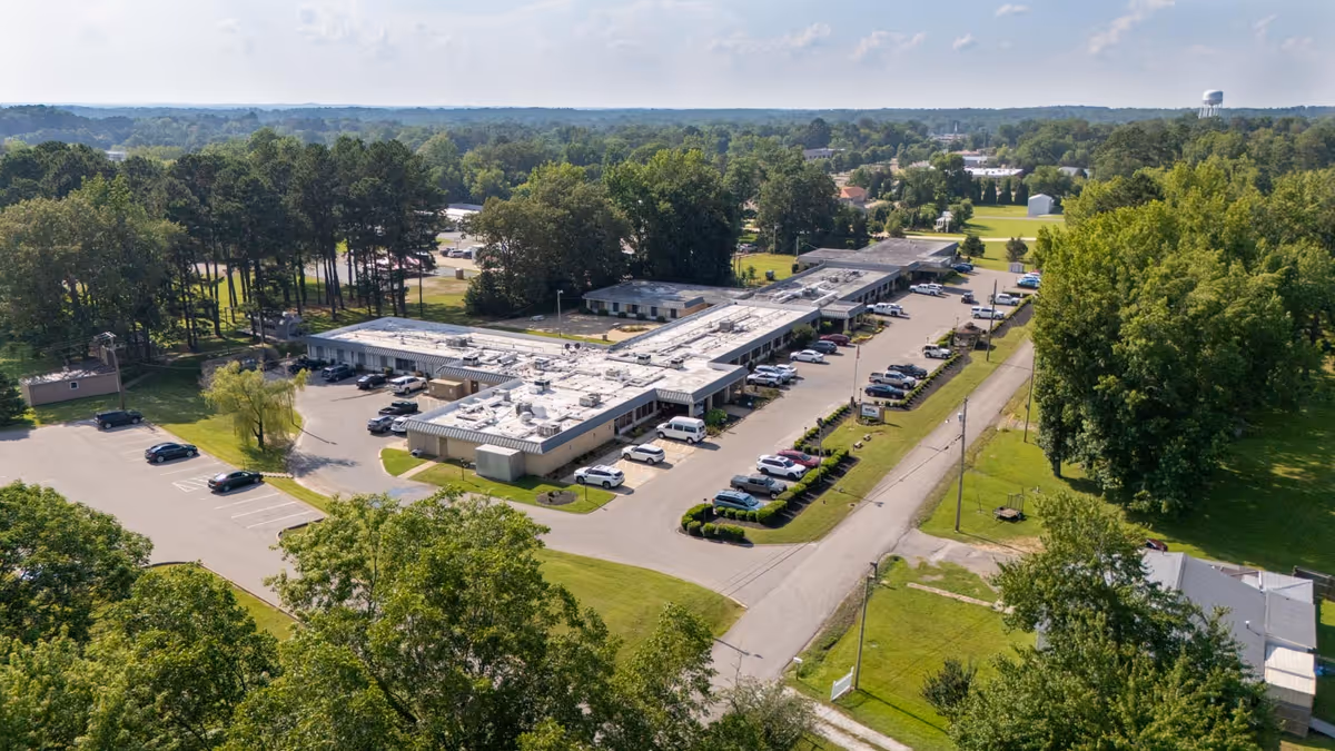 Aerial view of a single-story healthcare facility with parking lots, surrounding trees, and nearby roads.