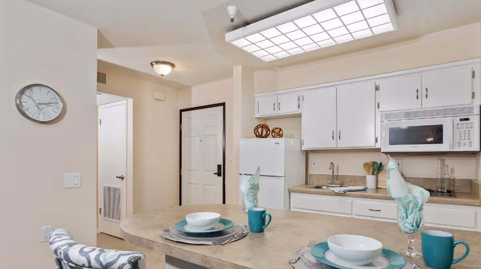 Kitchen interior featuring a countertop with place settings, white cabinets, microwave, refrigerator, and an entry door.