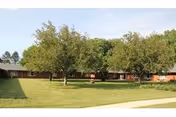 Single-story brick senior living building surrounding a green courtyard with trees and a sidewalk.