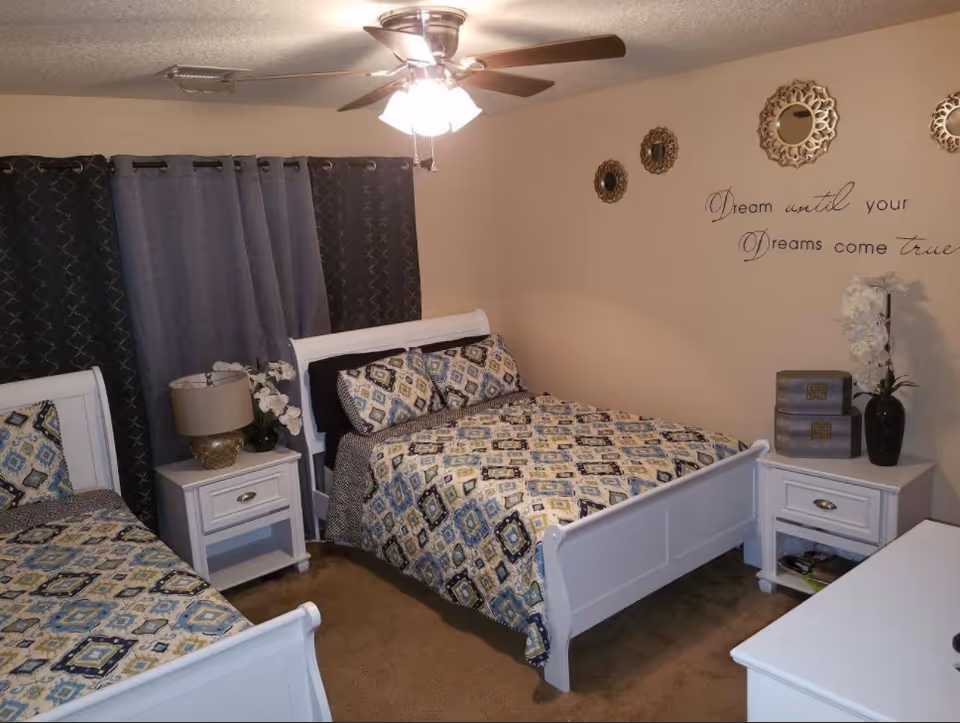 Two white beds with patterned bedding and nightstands in a softly lit bedroom.