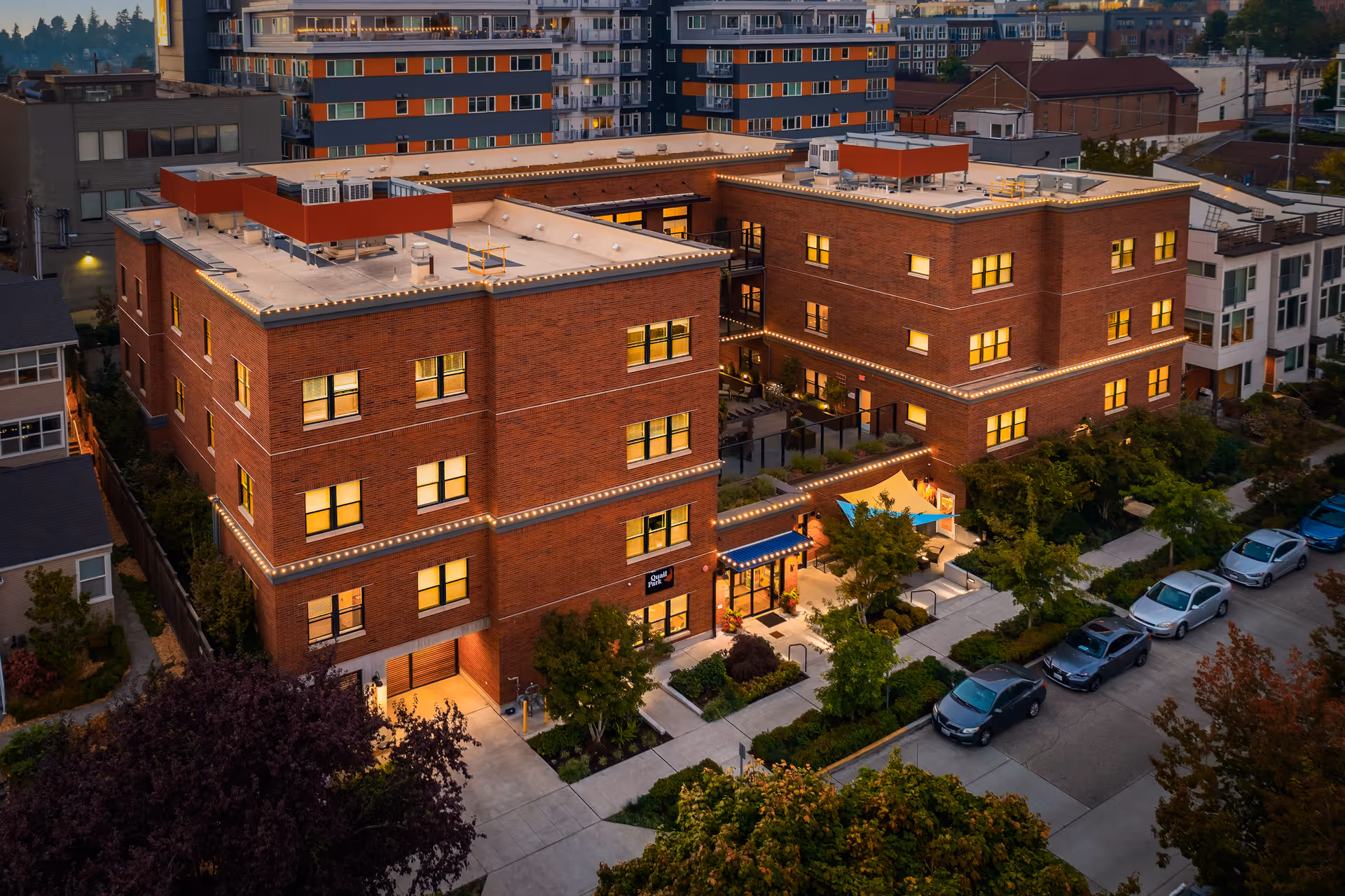 Aerial view of Quail Park of West Seattle exterior brick buildings with lit windows and entrance.