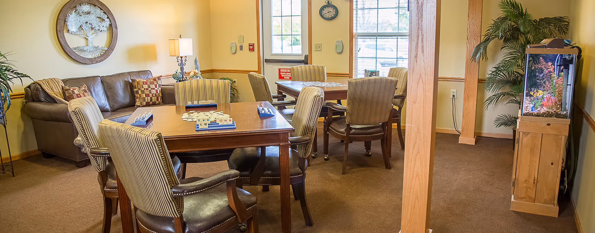Cozy senior living common room with tables and chairs, a sofa, and an aquarium.