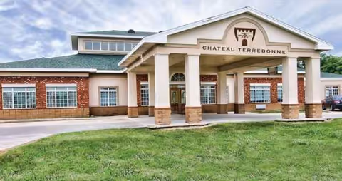 Exterior view of Chateau Terrebonne Health Care entrance with brick columns and lawn.