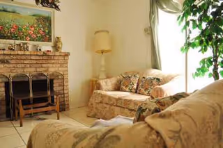 Cozy living room with floral sofas, a brick fireplace, and a tall floor lamp.