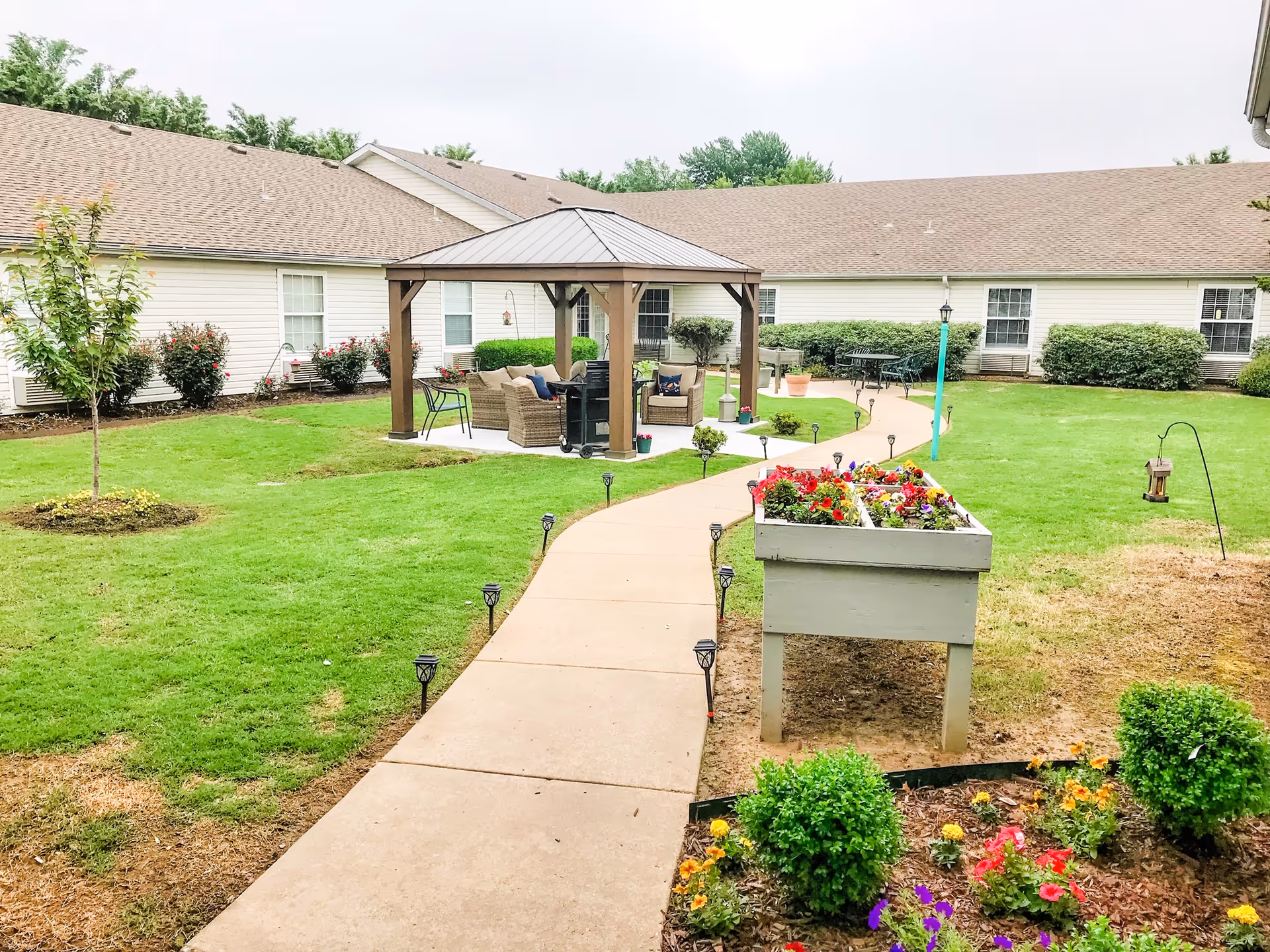 Landscaped courtyard with a gazebo, paved walkway, raised flower planter and surrounding single-story building.