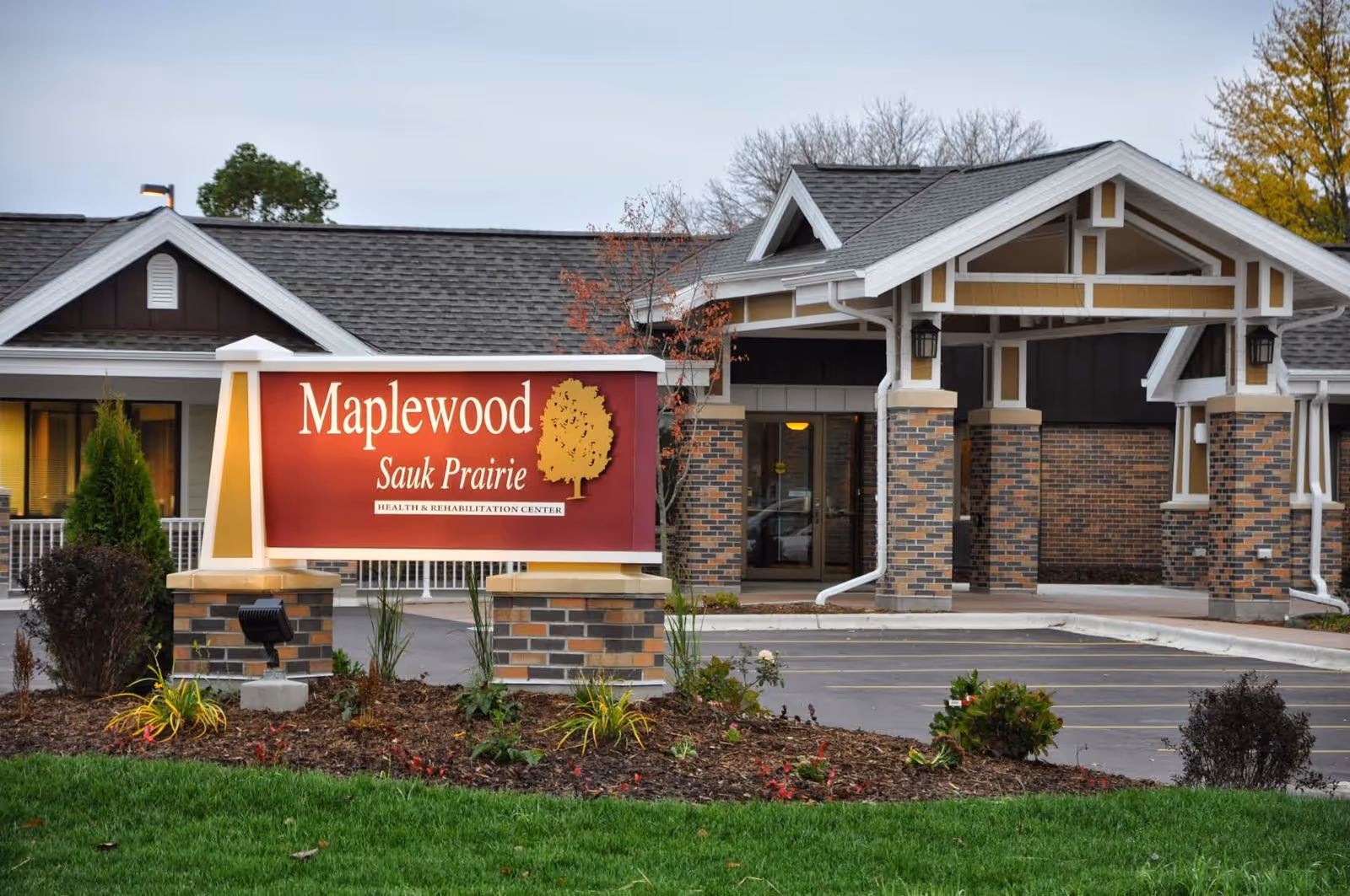 Front entrance and sign for Maplewood Sauk Prairie health and rehabilitation center with brick columns and landscaped grounds.