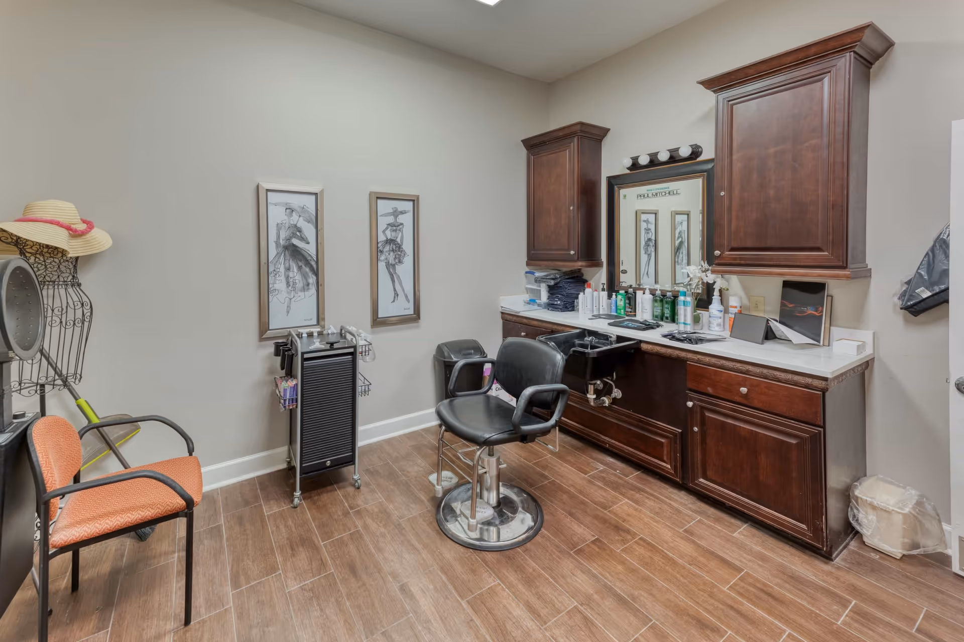 Interior salon room with a styling chair and sink, dark wood cabinets, mirror, and additional seating and decor.