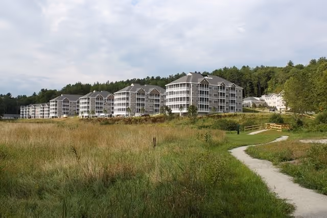 Multi-story senior living buildings set behind a grassy field with a winding path in the foreground.