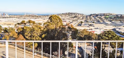 Balcony view from Bernal Heights Retirement Home overlooking trees, hills, and distant industrial area.