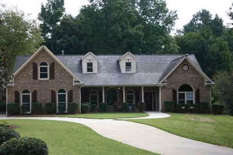 Brick senior living facility exterior with curved driveway, manicured lawn, and trees.