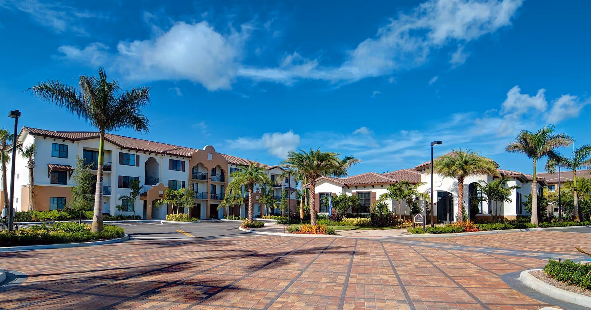 Wide exterior view of Upside Boca Raton senior living campus, with palm trees and blue sky.