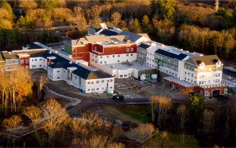 Aerial view of a multi-wing assisted living facility building on a wooded campus with surrounding grounds.