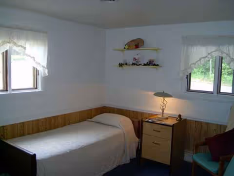 Small furnished bedroom in a senior care home with a single bed, nightstand, and lamp.