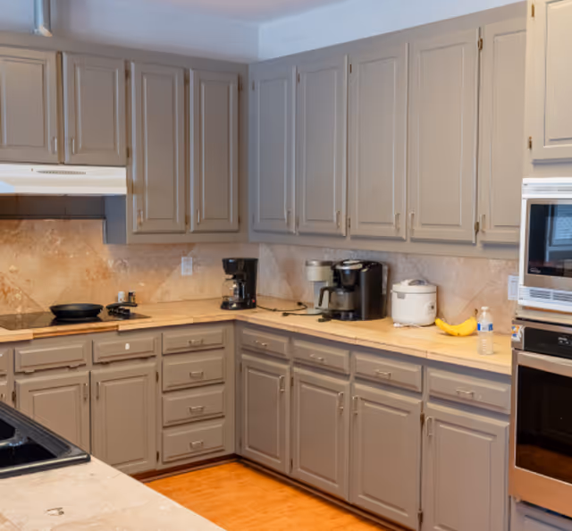 U-shaped kitchen with gray cabinets, beige countertops, and multiple small appliances.