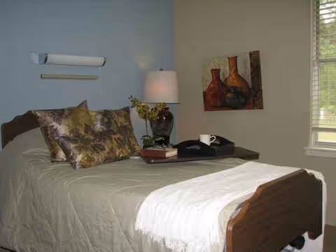 A neatly made bed with pillows, nightstand, lamp, and wall art in a bedroom.