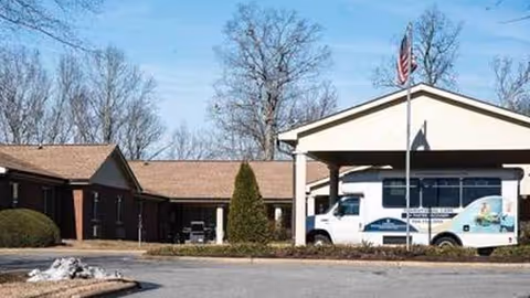 Exterior view of a senior living facility with a front entrance and parked shuttle bus
