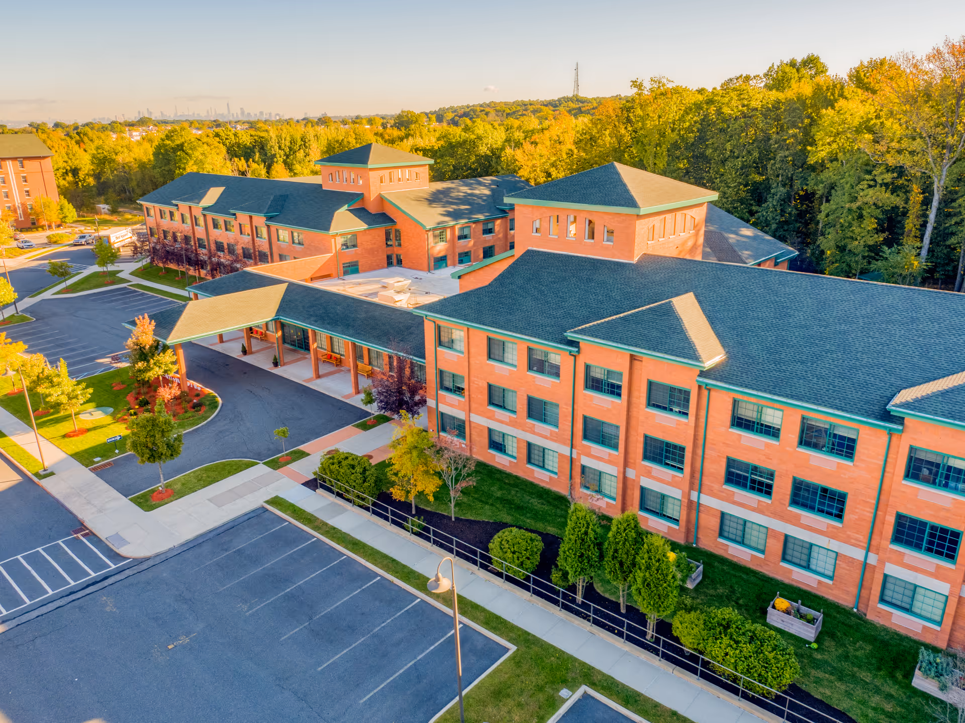 Aerial view of a large brick senior living building with a covered entrance, parking lot and landscaped grounds.