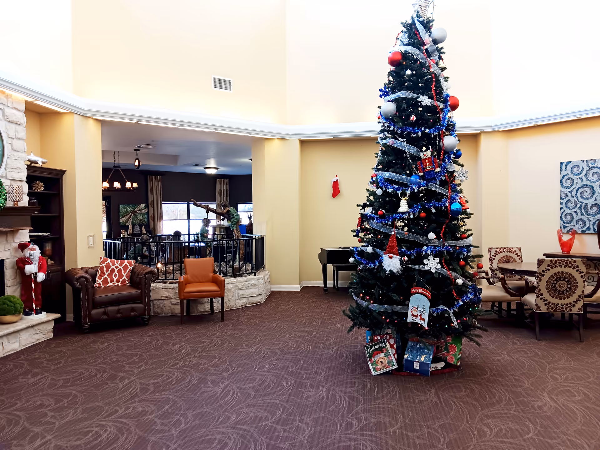 Spacious senior living common room with a large decorated Christmas tree and seating areas.