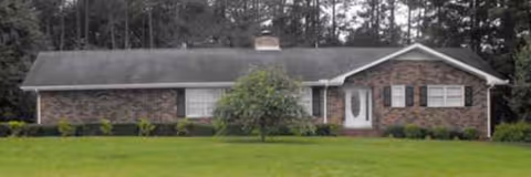 Single-story brick building with front lawn, shrubs, and trees in the background.