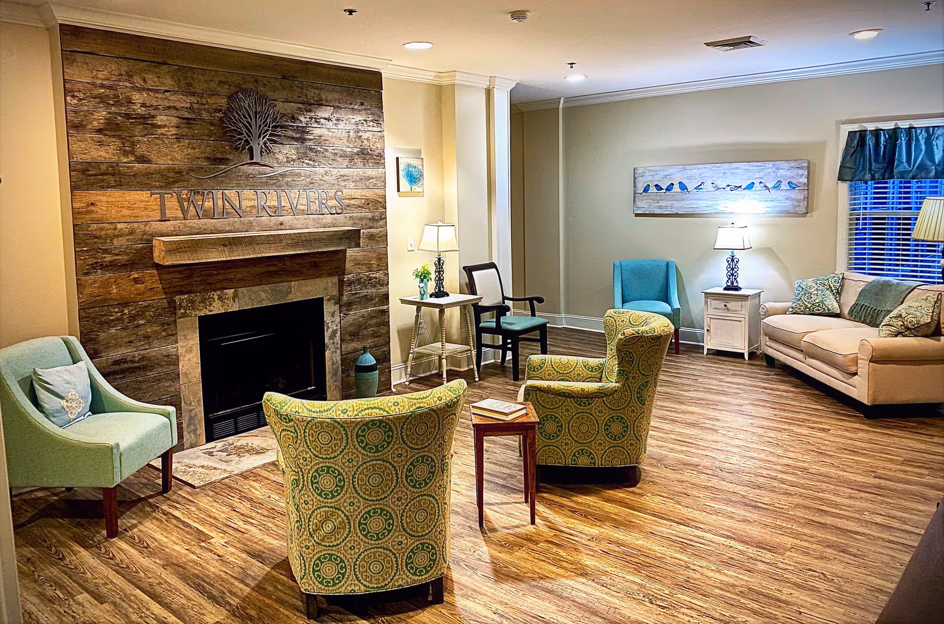 Cozy senior living lounge with fireplace, teal chairs, sofa, and contemporary decor.
