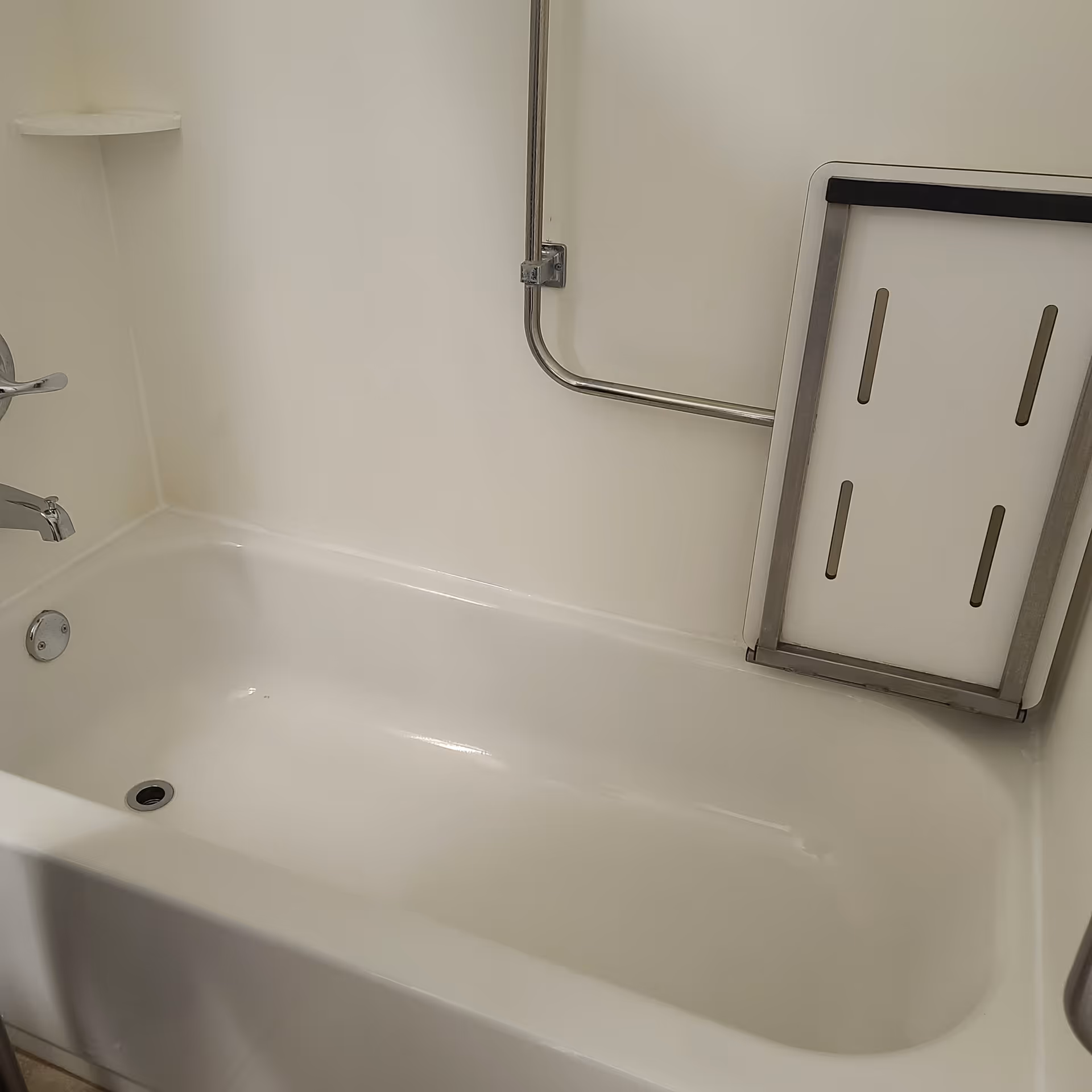 White bathtub with a wall-mounted grab bar and a folding shower seat attached to the wall.
