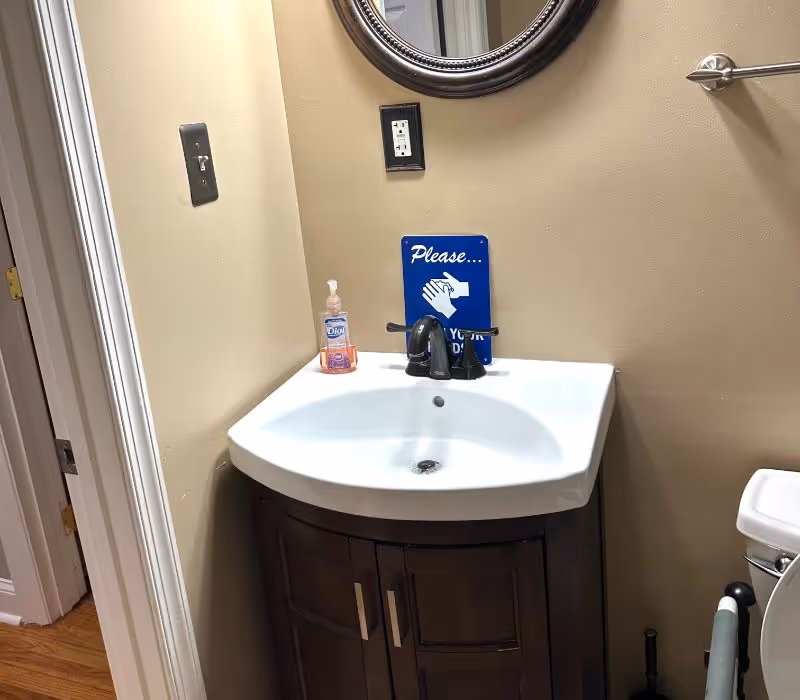 Small bathroom sink area with soap dispenser, mirror, and handwashing sign.