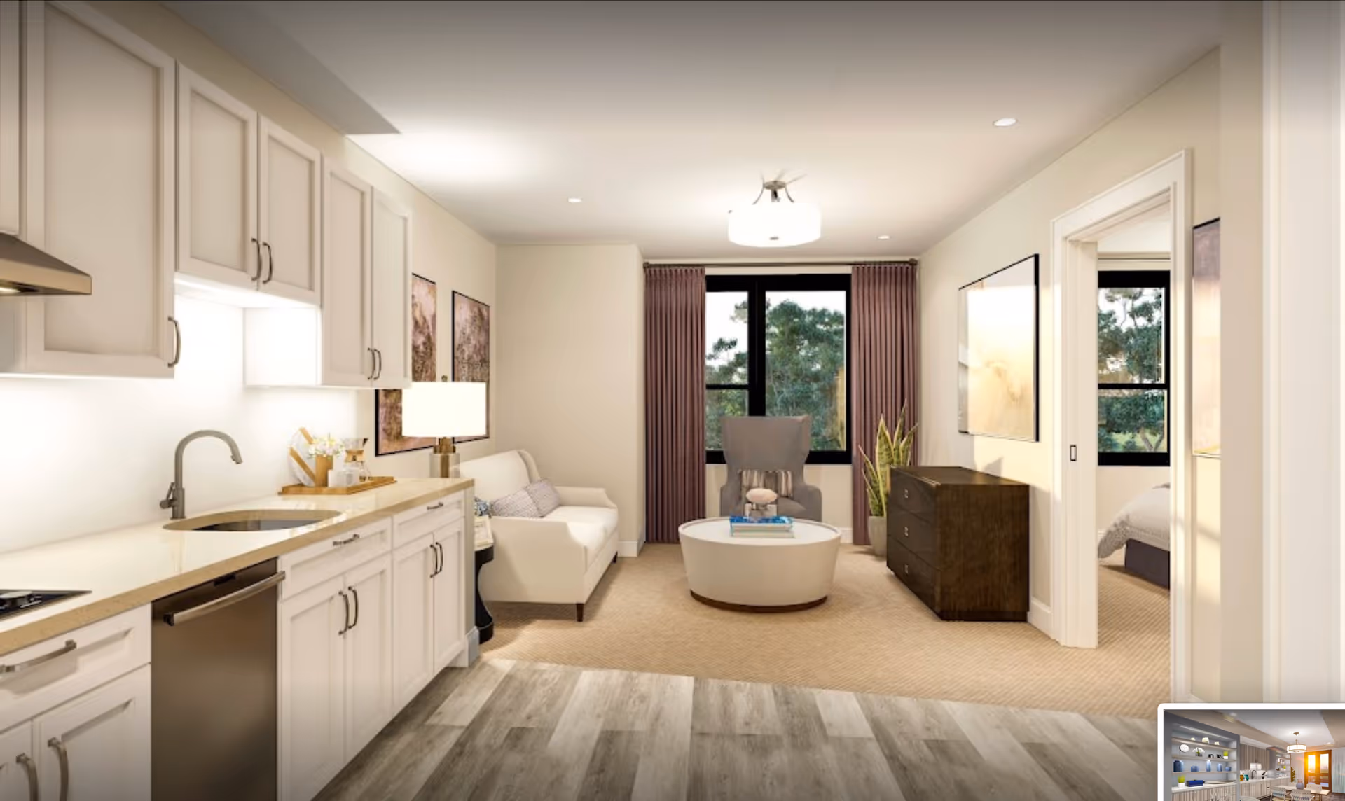 Open-plan living area with a compact kitchen on the left, a sofa and armchair around a round coffee table, and windows with curtains.