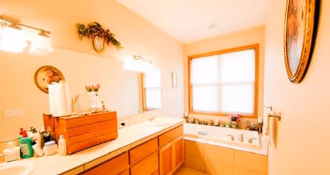 Bright bathroom with double sink vanity, cabinets, and tub by window.