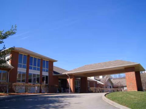 Exterior view of a brick senior living facility with a covered entrance and blue sky.