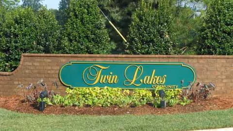 Brick wall sign reading Twin Lakes Community with landscaping in front of the entrance.
