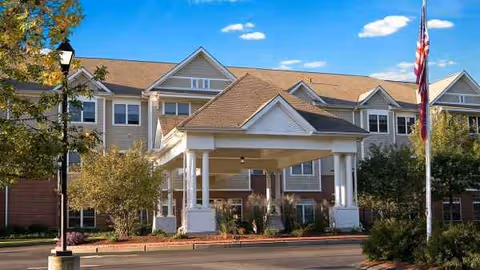 Front view of Atria Bay Spring Village with porte-cochere entrance and flag.