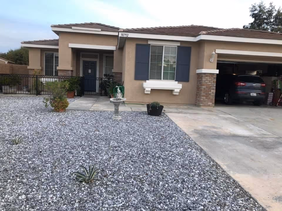Front exterior of a beige, single-story senior living facility with a gravel yard and driveway.