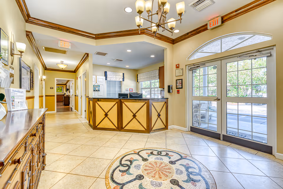 Bright reception lobby with a tiled floor and decorative medallion, a front desk, and glass double entry doors.