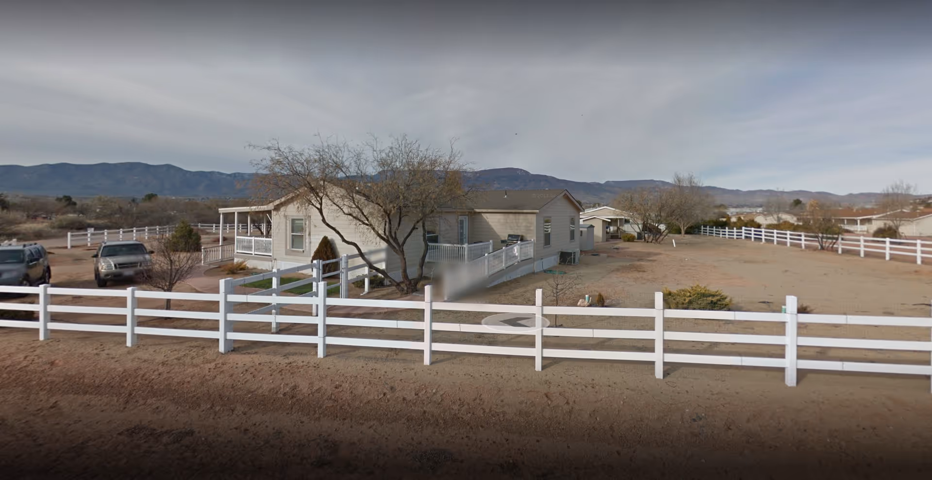 Single-story facility with white fencing, desert landscape, and distant mountains.