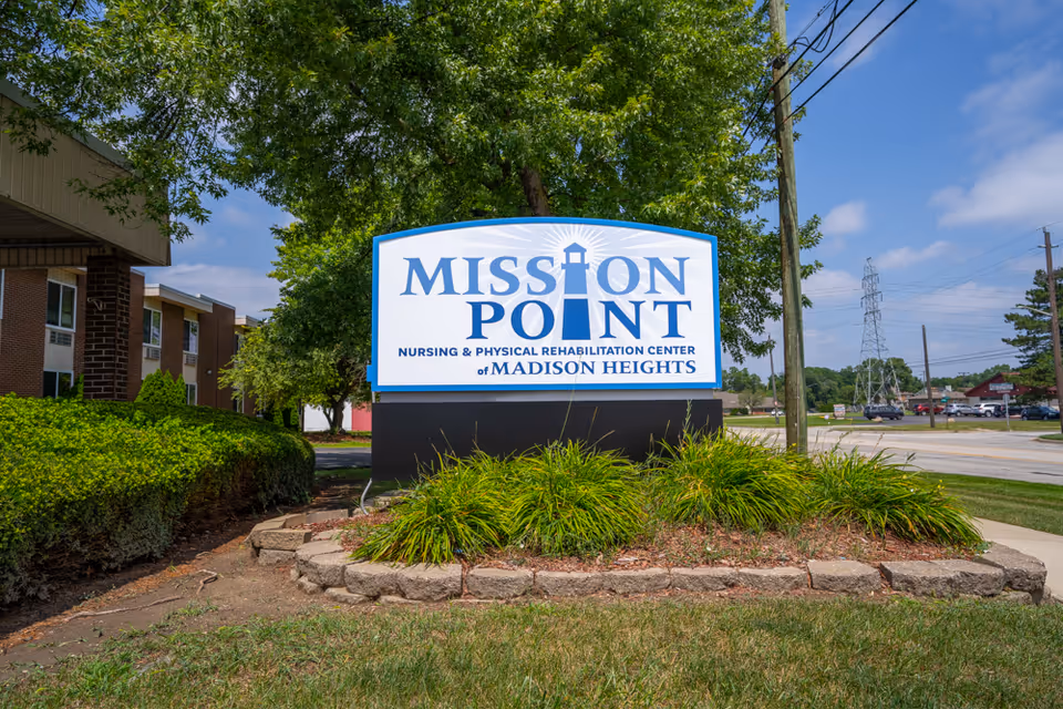 A large blue-and-white sign for Mission Point Nursing & Physical Rehabilitation Center of Madison Heights stands in landscaped greenery outside the facility.