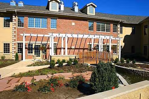 Exterior view of Brookestone Meadows showing brick building, pergola, and landscaped courtyard with water feature.