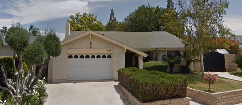 Front exterior of Carmen's Care Manor, a single-story senior living facility with a garage and shrubs.